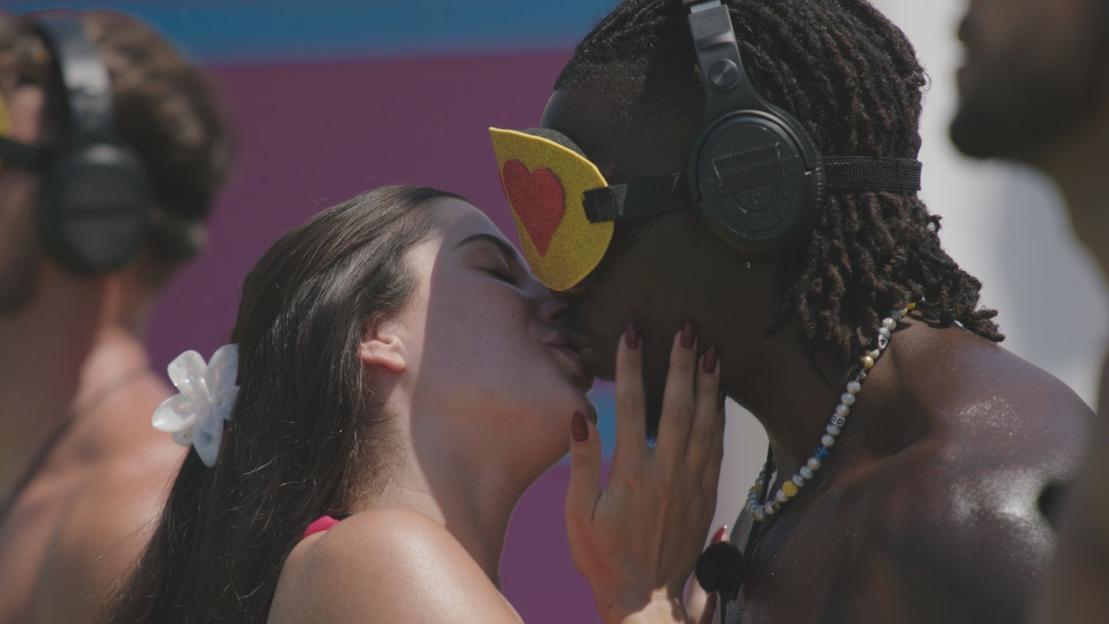Couple kissing while one wears a heart-shaped eye mask.