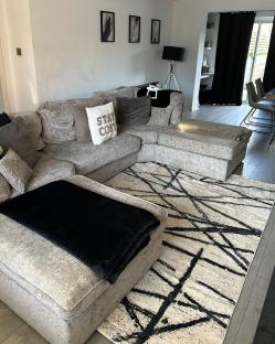 Large grey L-shaped sofa with black throw blanket on a black and white rug.