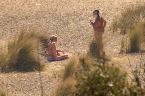 Two nude individuals on a beach.
