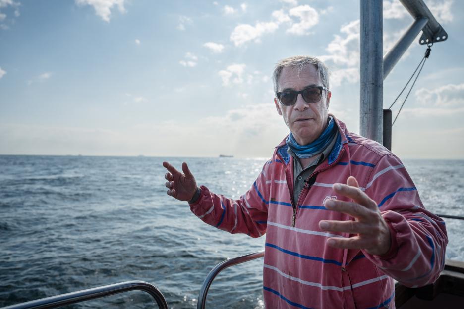 Man in sunglasses gesturing on a boat at sea.