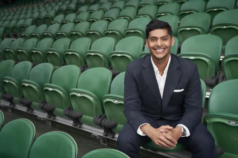 Man in suit sitting in empty green stadium seats.