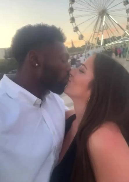 Couple kissing in front of a Ferris wheel.