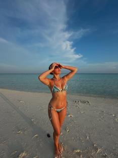 Woman in bikini on beach looking at sky.