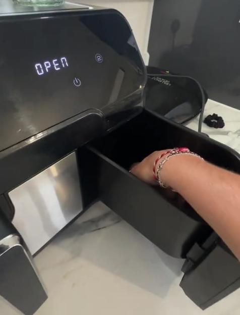 A hand opening the drawer of a black air fryer.