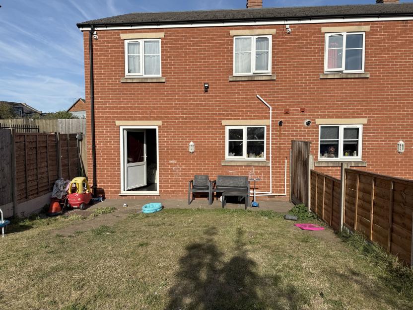 Back garden of a brick house with toys and patio furniture.