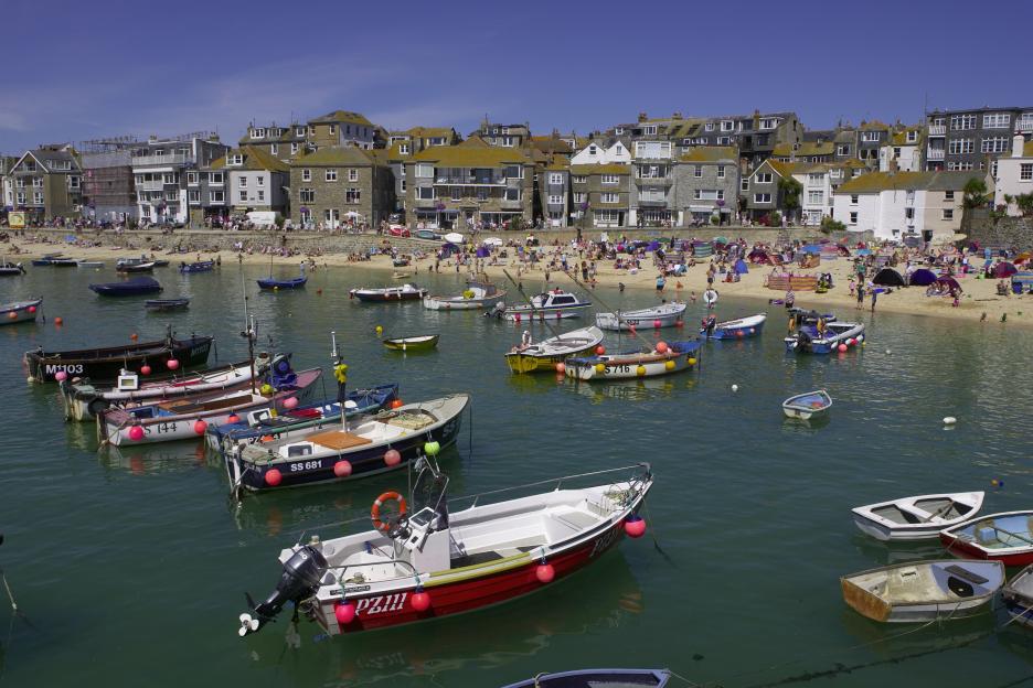 Boats in a harbor with a crowded beach and buildings in the background.