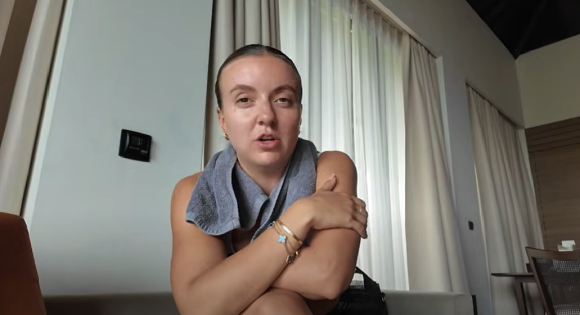 Woman speaking to camera in hotel room.