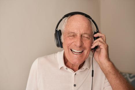 Happy senior man singing along to music with headphones.