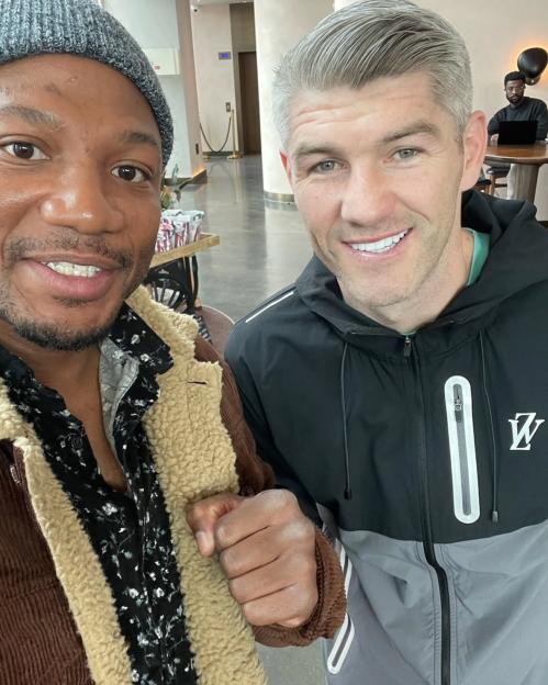 Photo of two men smiling, one in a brown jacket and the other in a gray and black jacket.