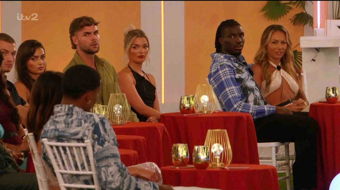 Love Island contestants seated at tables.