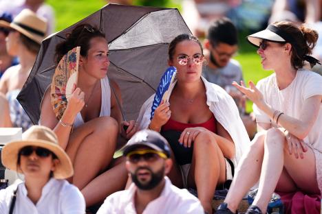 Spectators using fans and umbrellas to stay cool at Wimbledon.