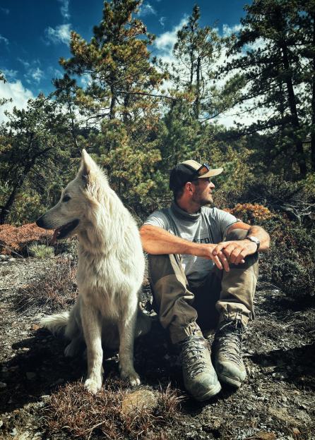 Man and white dog sitting in the woods.