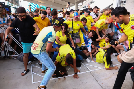 A crowd of soccer fans, many wearing yellow and blue jerseys, pushing and shoving near a barrier.
