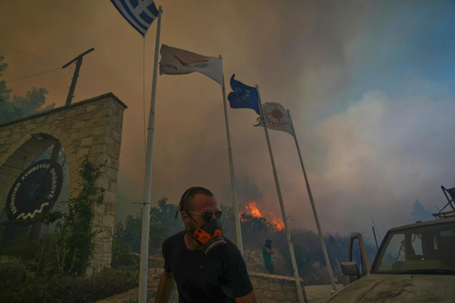 A man wearing a respirator mask stands near a wildfire in Omodos, Cyprus.
