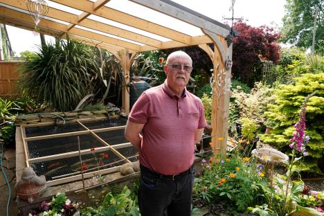 Man standing in his garden next to a fish pond.