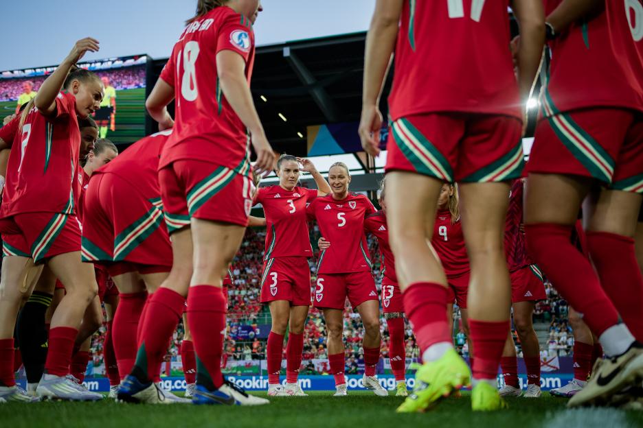 Wales women's soccer team huddles on the field.