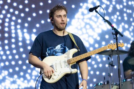 Sam Fender performing at a music festival, playing an electric guitar.