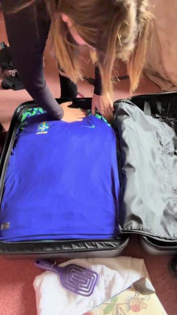 Person packing a blue shirt into a suitcase.