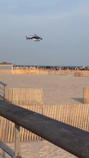 Police helicopter over a beach with a crowd of people.