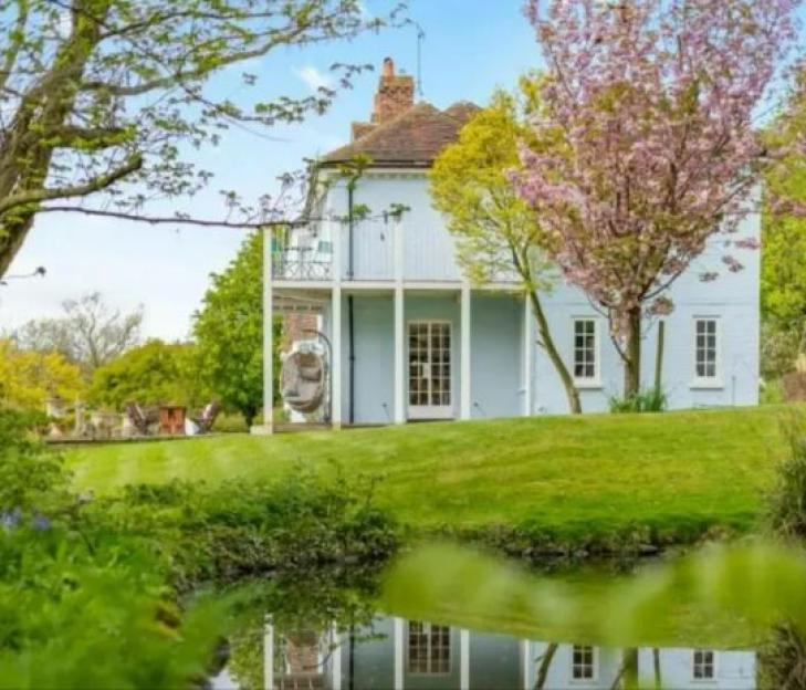 Paul O’Grady's light blue mansion with a pond in front.