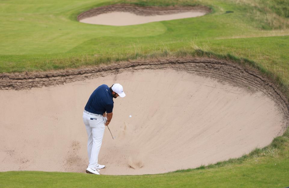 Scottie Scheffler hitting a golf ball out of a sand trap.