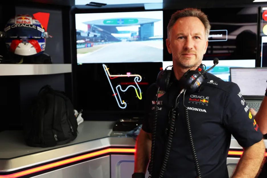 Man in Red Bull Racing uniform in front of monitors showing race track.