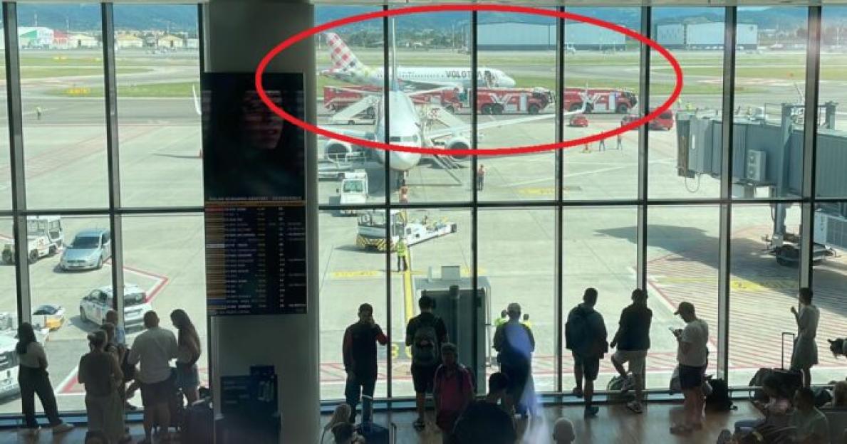 Airport passengers viewing a plane on the tarmac with emergency vehicles.