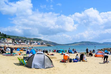 Beachgoers enjoying sunny weather at Lyme Regis, Dorset, UK, during the Fossil Festival.