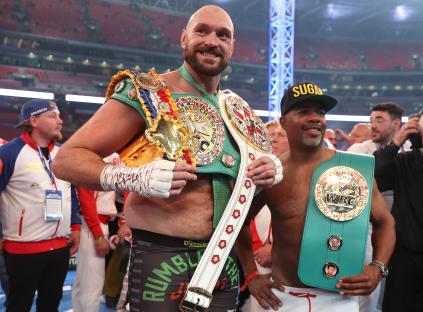 Tyson Fury celebrating a boxing victory with championship belts.