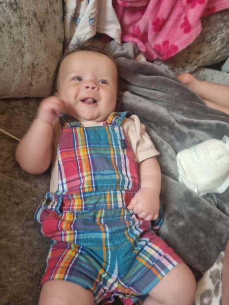 Smiling six-month-old baby in plaid overalls.