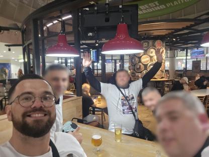 A group of men at an airport bar, one man is raising his hands.