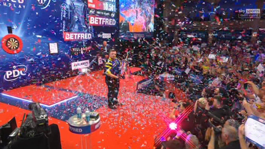 Darts player on stage amidst confetti and cheering crowd.