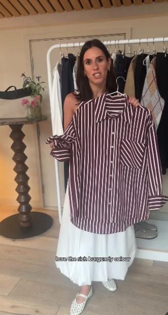 Woman holding up a burgundy and white striped shirt.