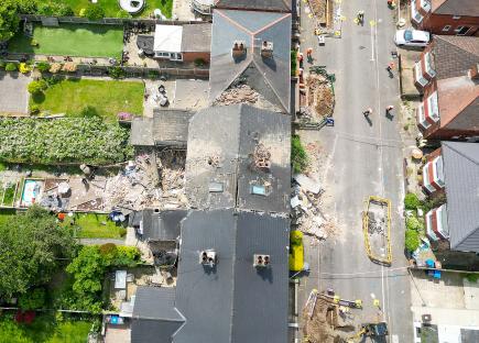 Aerial view of a house damaged by a suspected gas explosion, with emergency responders on scene.