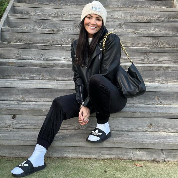 Martine McCutcheon sitting on steps wearing black leather jacket and Adidas slides.