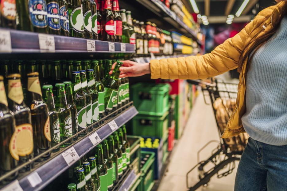 Woman selecting a beer bottle from a supermarket shelf.