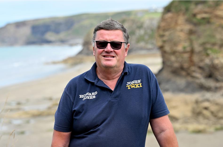 Howard Jones, a former journalist and current taxi driver, stands near the coast.