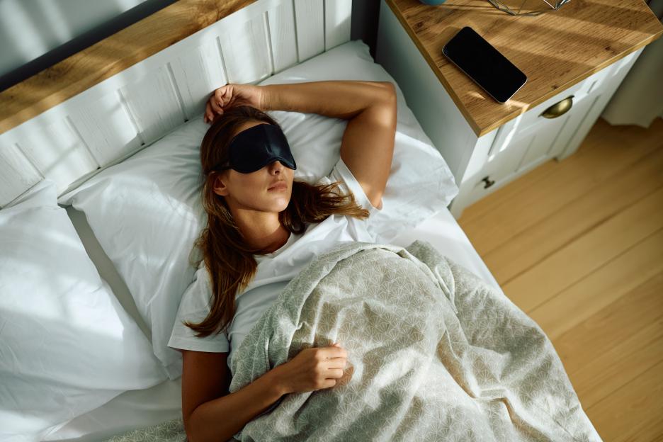 Woman sleeping in bed wearing a sleep mask.