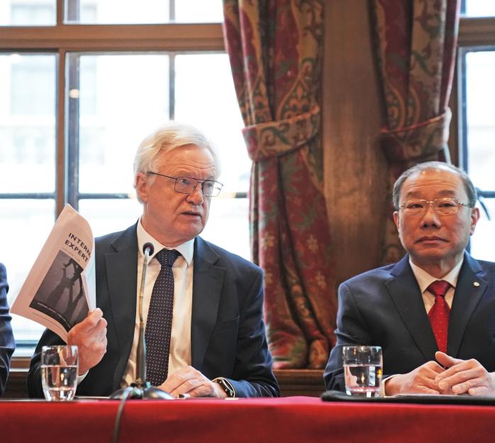 Three men at a press conference; one holds a report.
