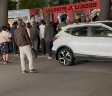 Screenshot of a crowd of people gathered around a bus and a white SUV.