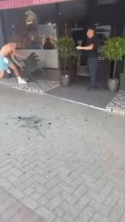 A shirtless man throws a chair outside a restaurant while a man in a dark shirt watches.