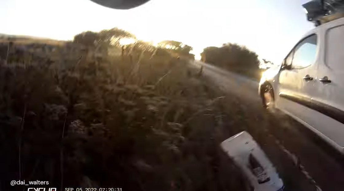 Screenshot of a person cycling past a white van at sunset.