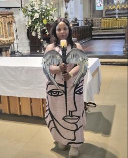 A woman in a church holds a candle with angel wings.