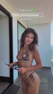 Woman in brown bikini holding sunglasses on balcony.