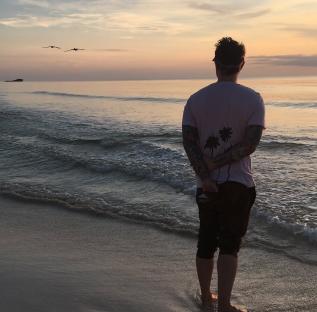 Man standing on beach at sunset, facing the ocean.