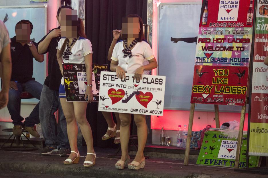 Women in Pattaya, Thailand, hold signs advertising a bar.