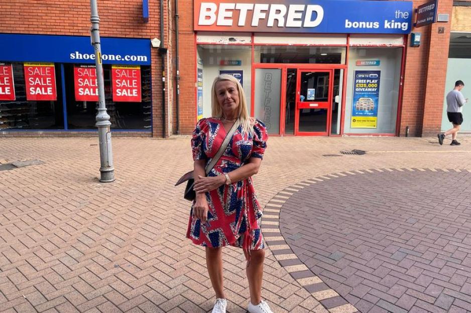 Woman in Union Jack dress outside a Betfred betting shop.