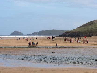 Crowded beach with people and surfboards.