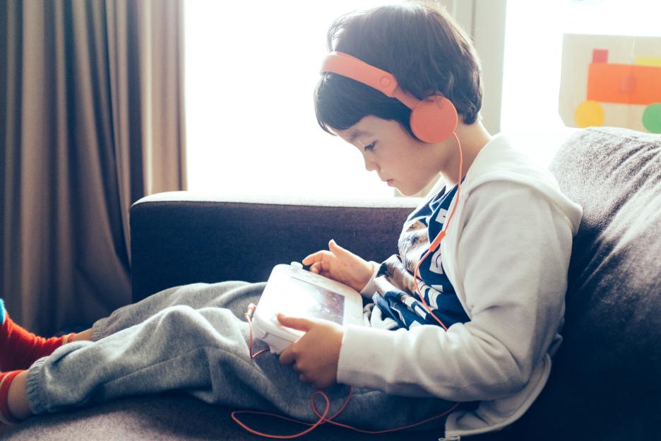 A young boy wearing headphones, holding a computer game console.