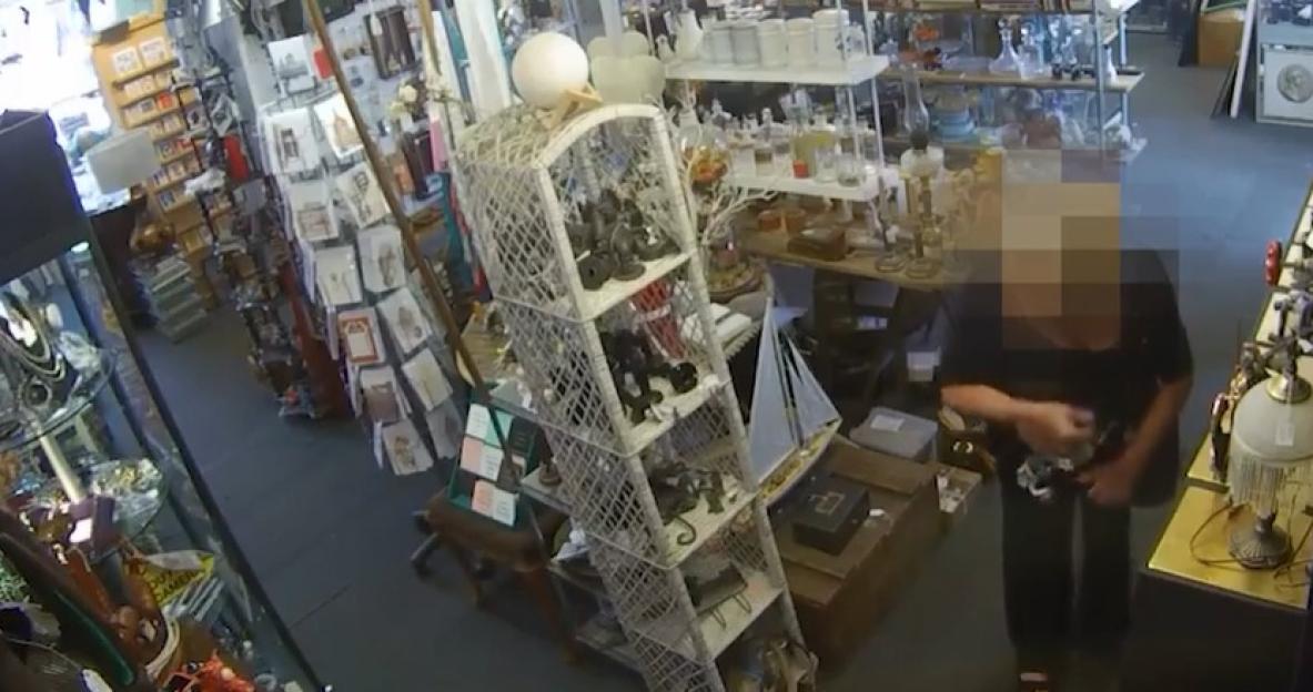 Security camera footage of a shop interior; a person is examining items on a shelf.